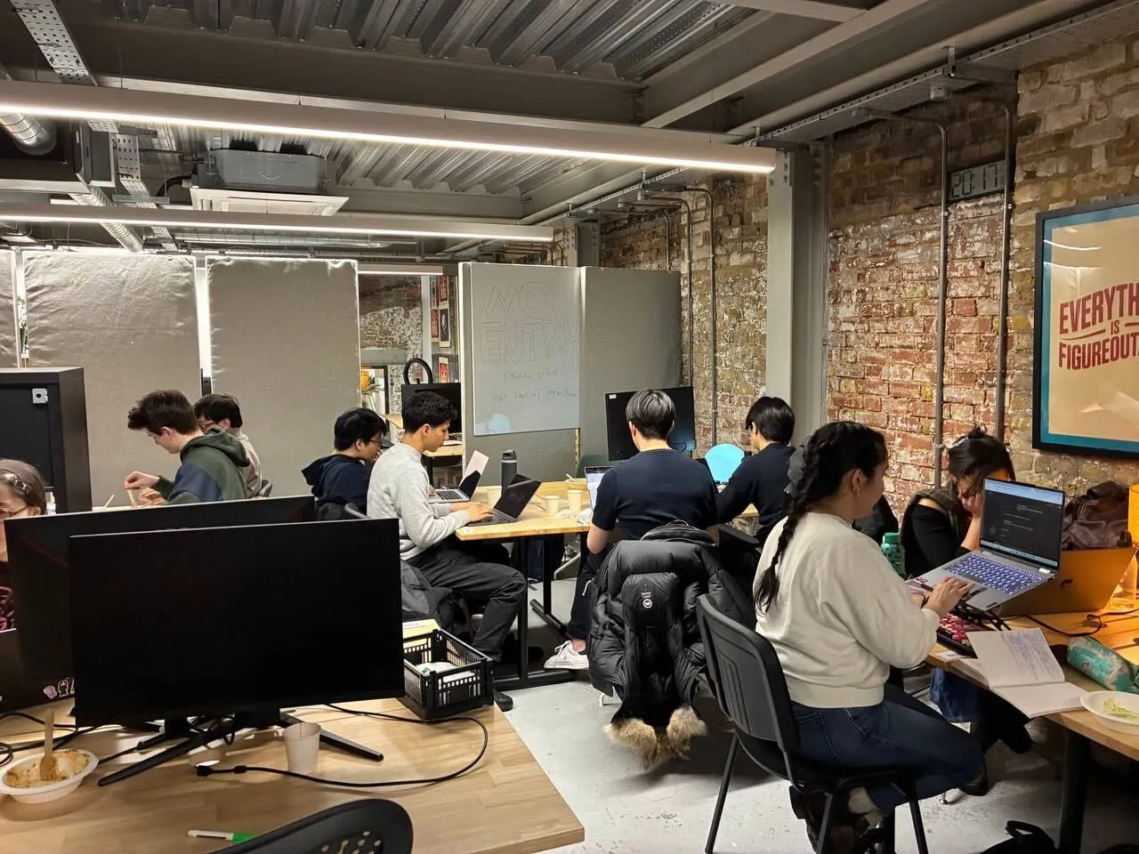 Builders at laptops around shared desks in a brick-walled London venue